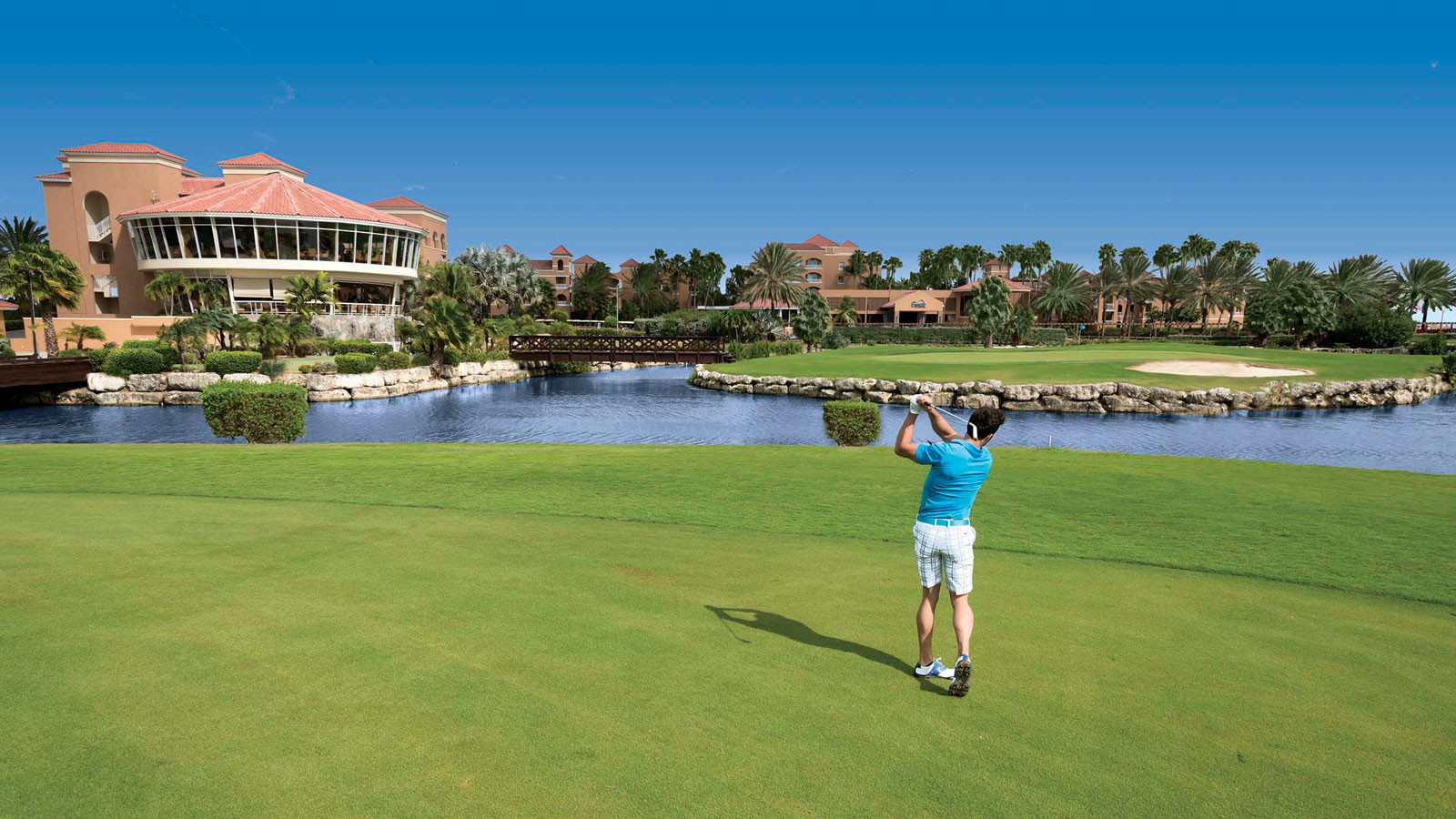 Sân golf tại Divi Village Golf & Beach Resort ở Aruba với thảm cỏ xanh mướt và hồ nước nhân tạo, tạo nên một không gian thư giãn và lý tưởng cho những người yêu thích golf.